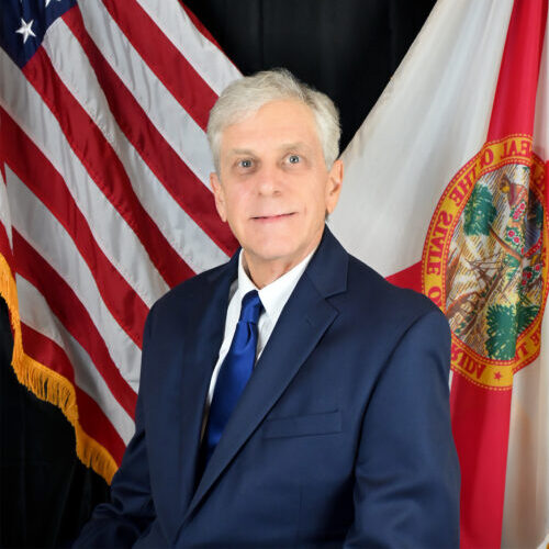 A person wearing a suit and tie standing in front of a flag
