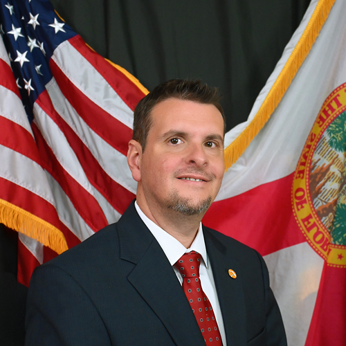 A person wearing a suit and tie standing in front of a flag
