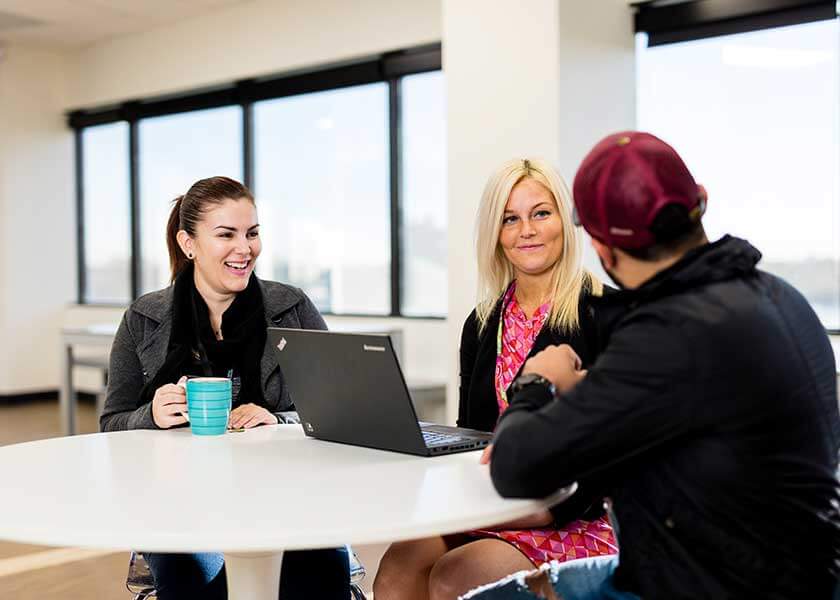 A group of people sitting at a table looking at a laptop